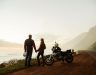 Man and woman watch sunset next to motorcycle