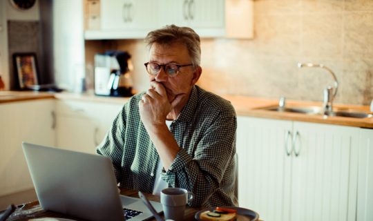 Man sitting at kitchen table contemplating his computer.
