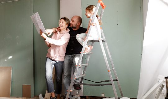 A couple and their young child look at plans for a renovation.