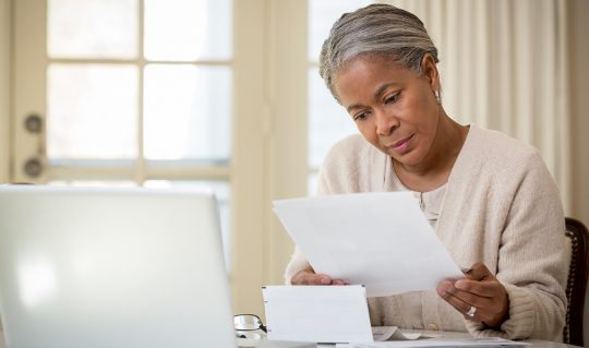 A woman looks through her financial paperwork to complete an online loan application at home instead of going to the bank to complete one in person.
