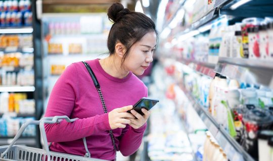 Woman browses groceries with phone in hand